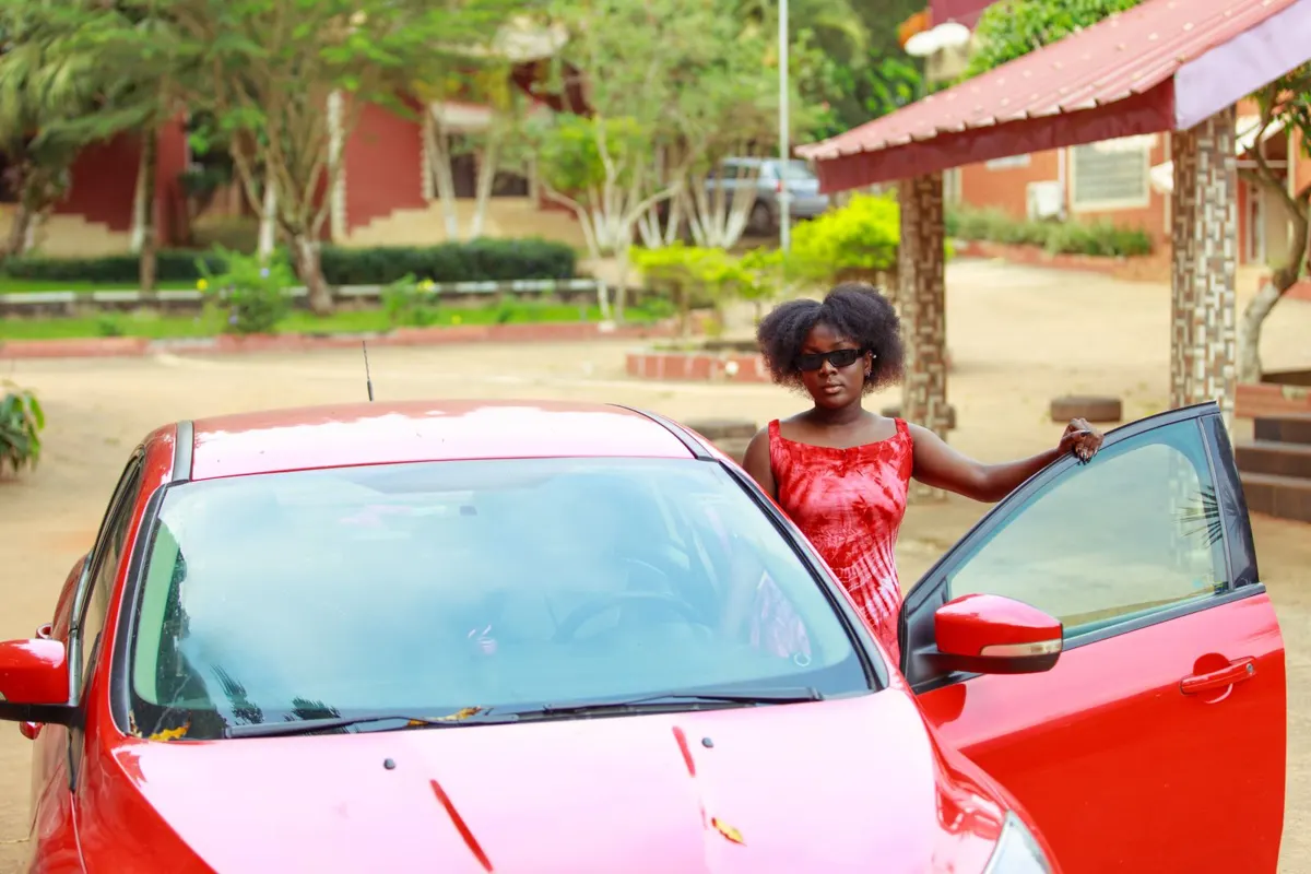 Woman standing proudly beside her red car with the door open